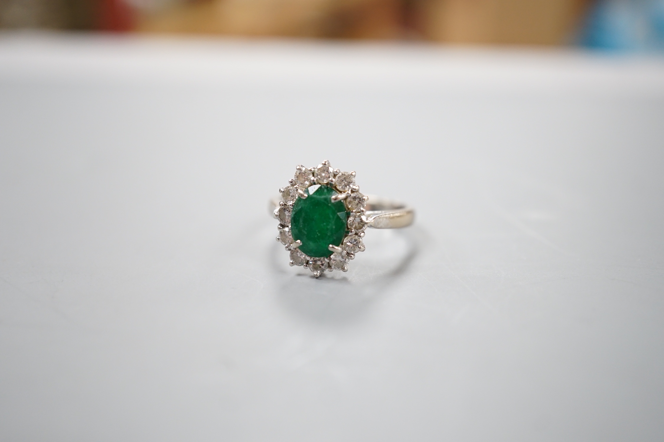 A modern 18ct white gold emerald and diamond set oval cluster ring, size O, gross weight 4.6 grams.